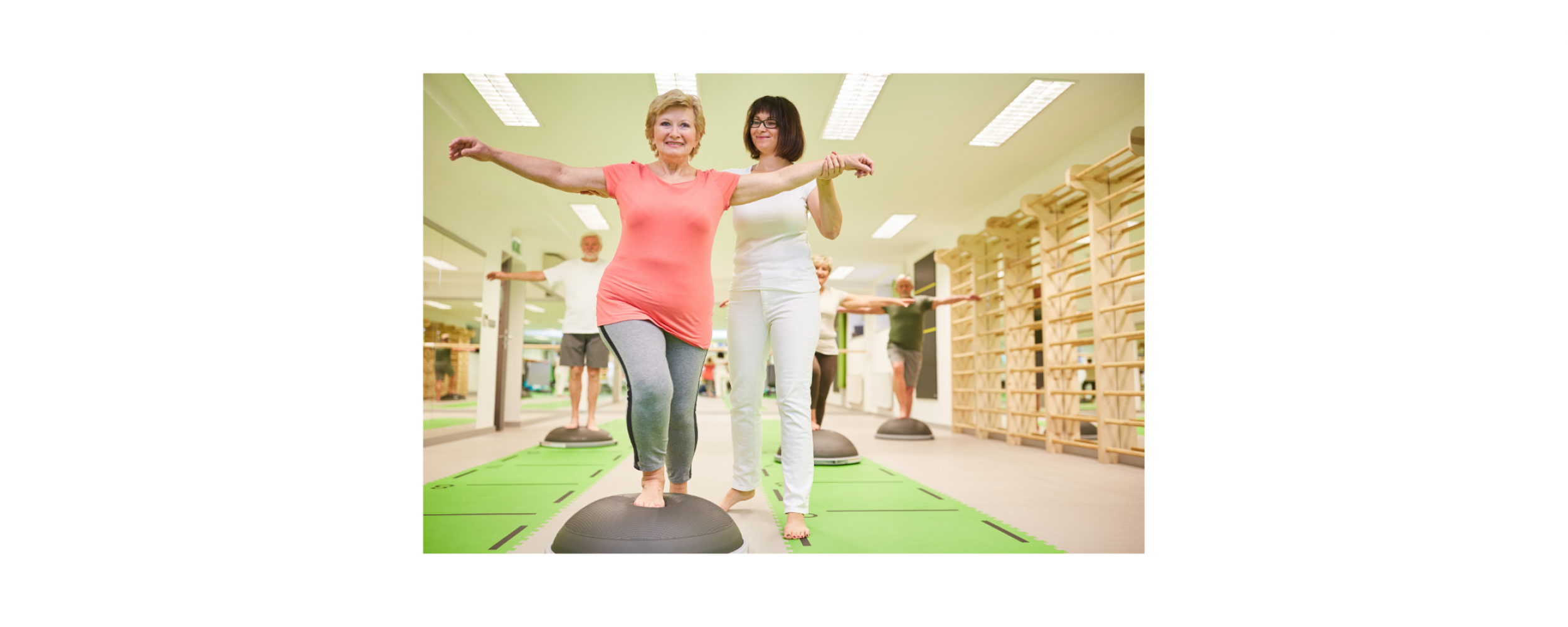 Trainer helps senior woman with balance training on the Bosu Ball in a fitness class