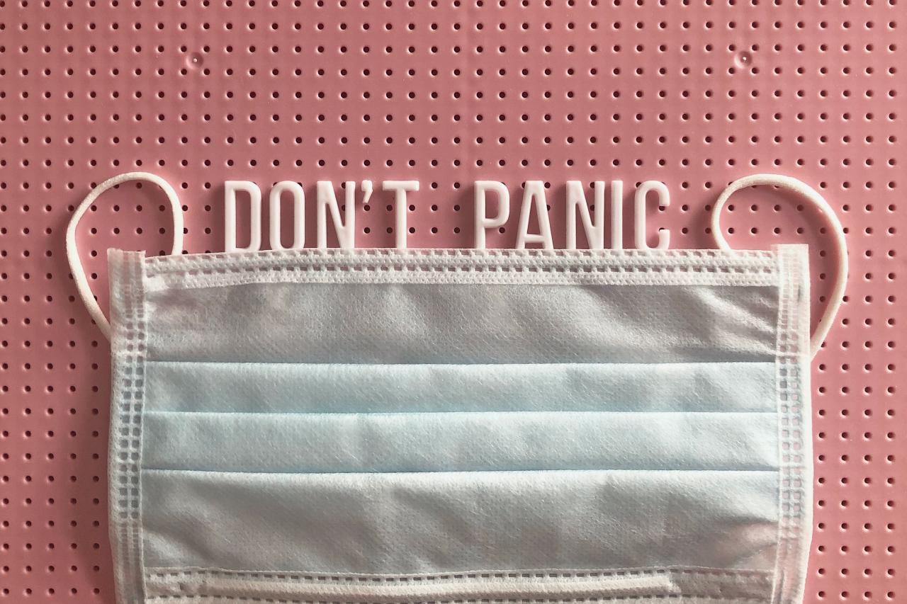 a face mask on a red background with the words "don't panic" written above the mask