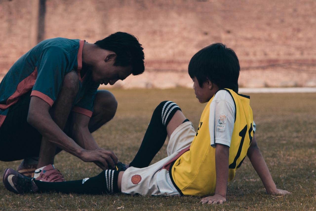 a coach crouches to look at the leg injury of an athlete