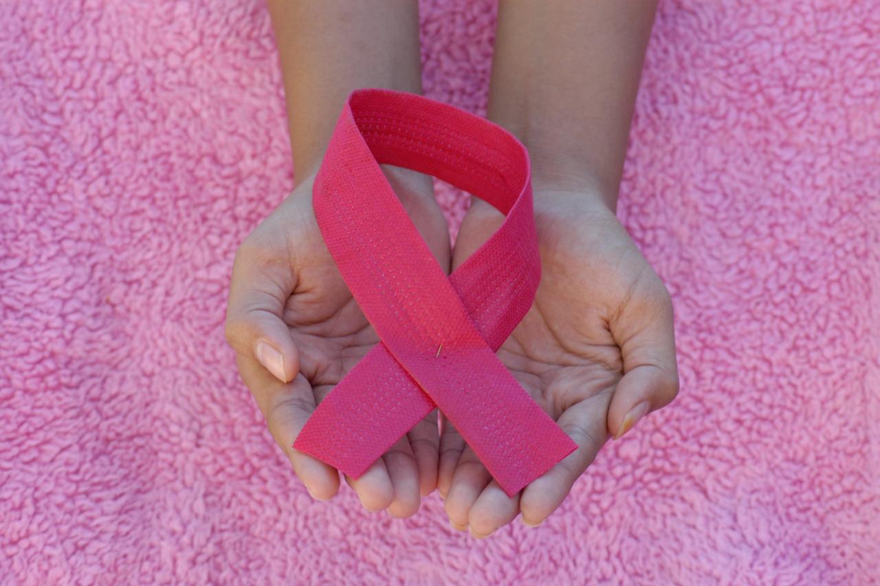 a pair of hands holding a pink ribbon 