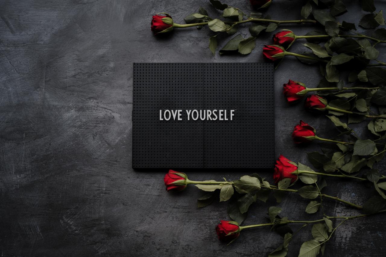 a slate with the text "Love Yourself" on it with red roses stacked next to the slate