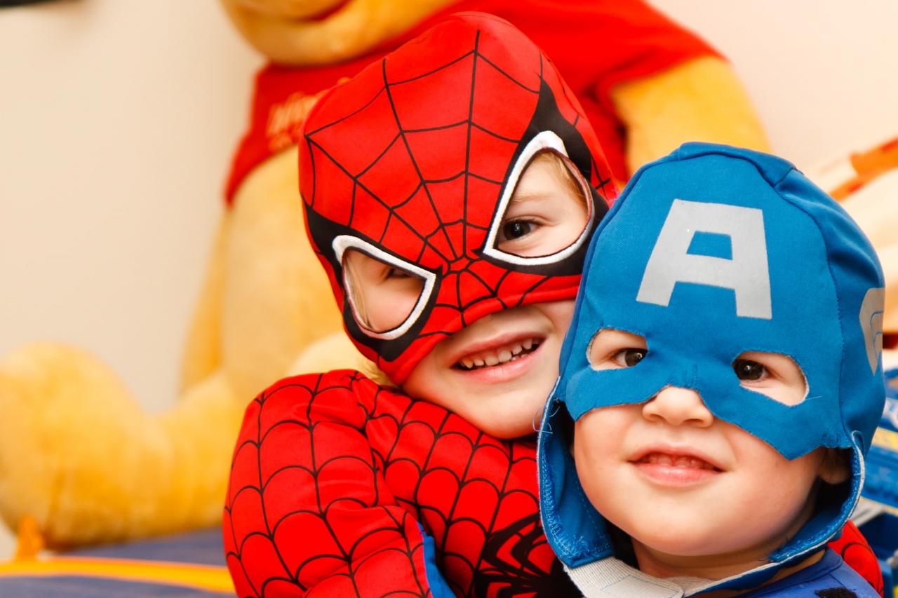 two children, one dressed as Spiderman, and another as Captain America, smile at the camera