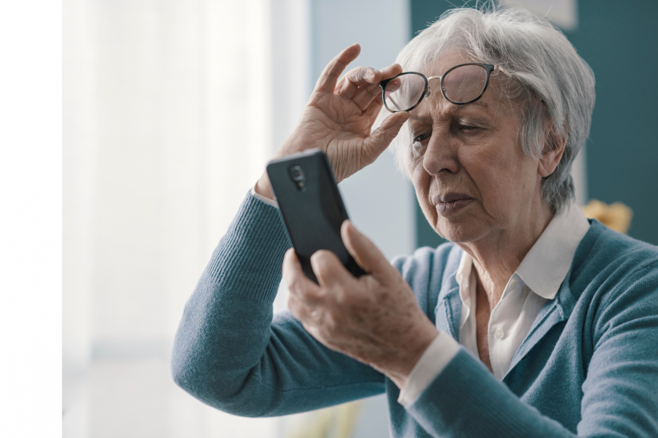 Elderly woman removing her reading glasses to see her cell phone screen.