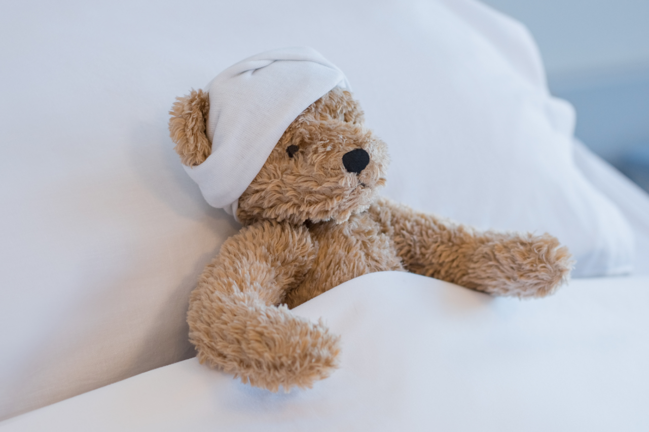 Teddy Bear tucked into bed with a bandage on it's head.