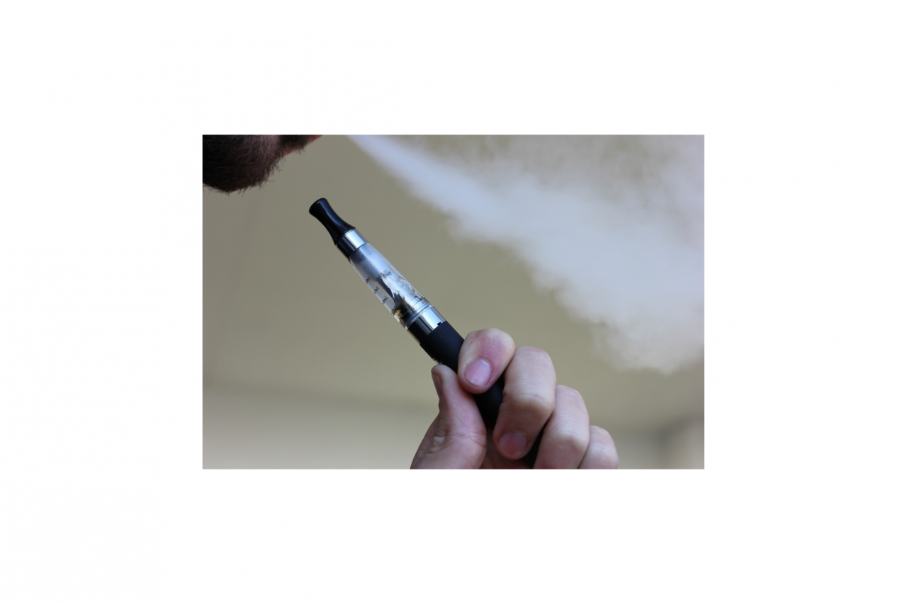 Person holding a vaping/e-cigarette pen while blowing out smoke from their mouth