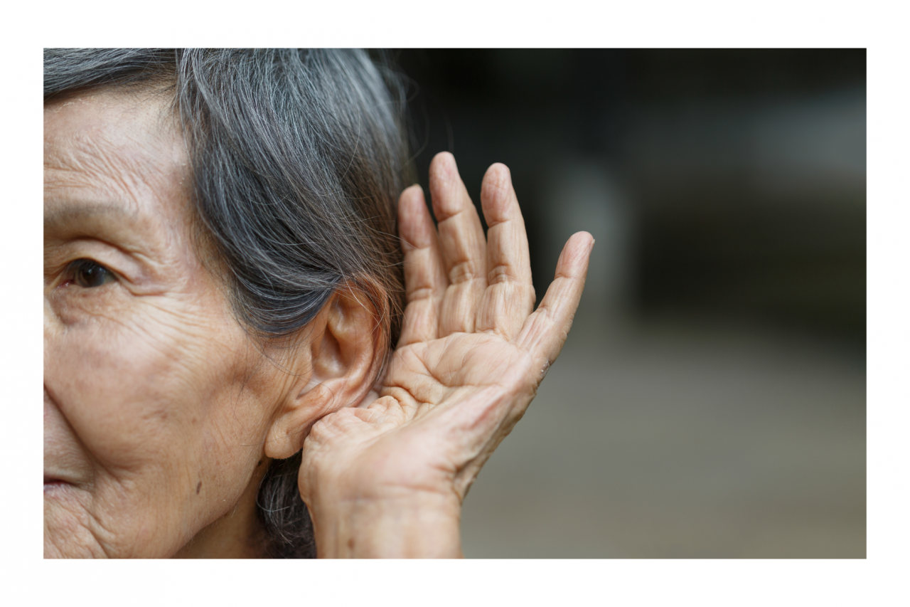 Older woman holding one hand up and cupping it around her ear, trying to hear.
