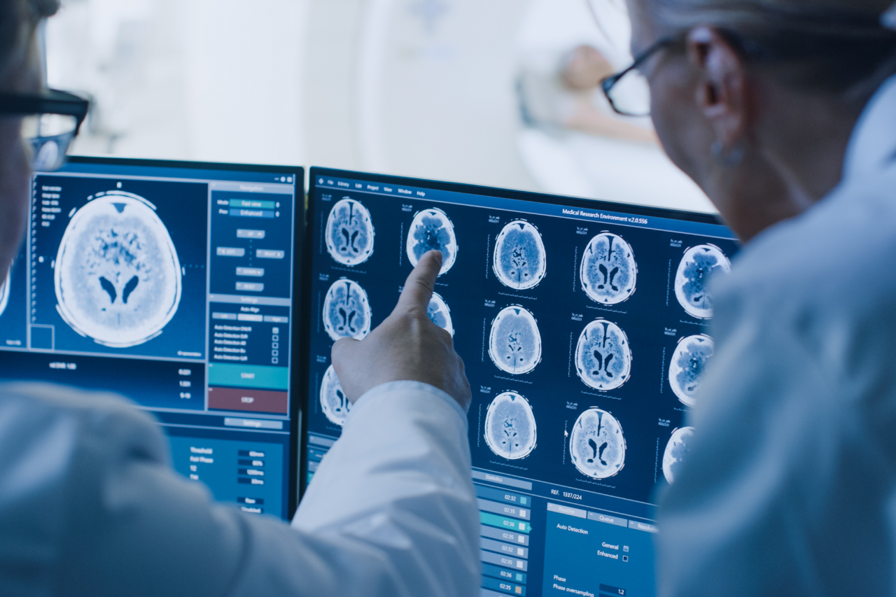 Doctor and radiologist discuss diagnosis while watching procedure and monitors showing patient's brain scan results