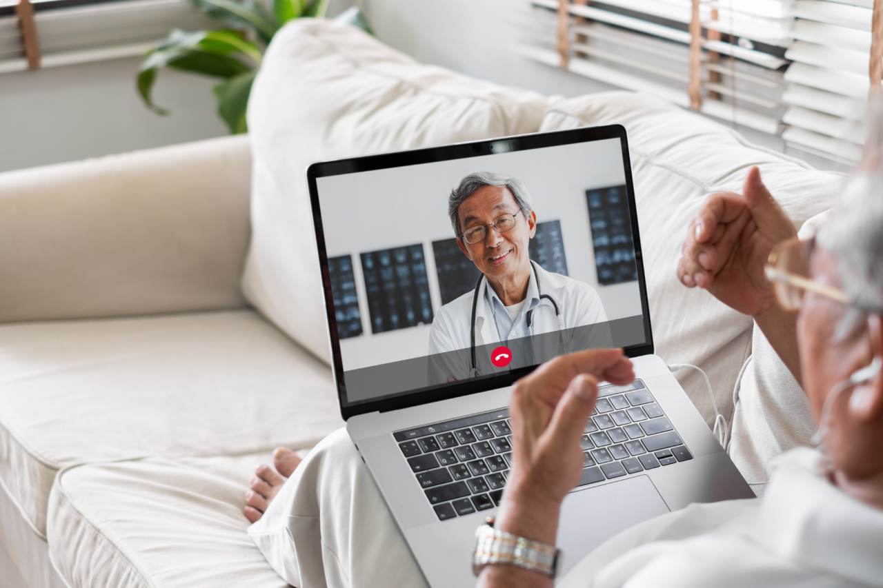 Elderly man having a telemedicine/telehealth video call with his healthcare provider using his laptop at home on his couch