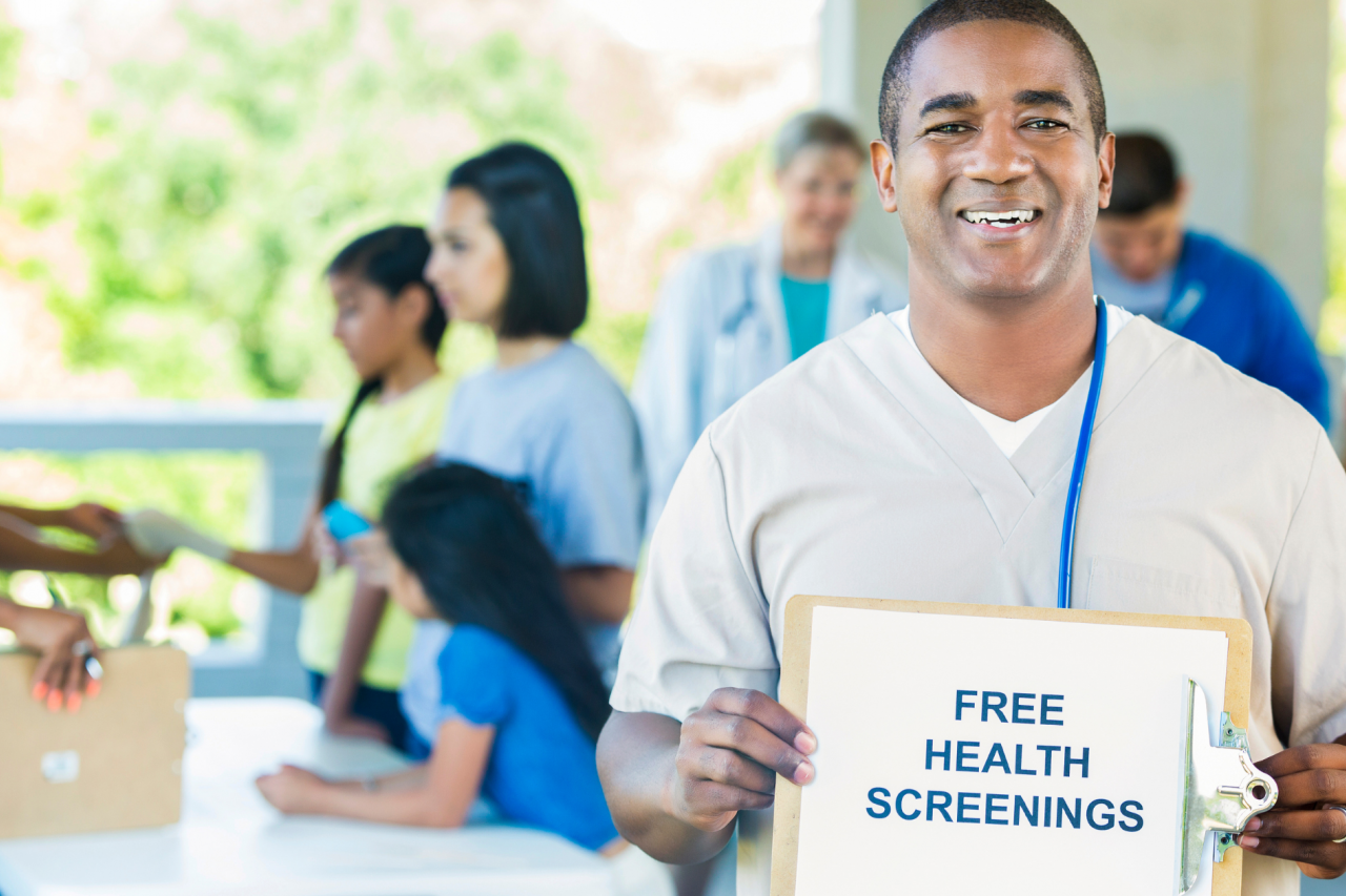 A healthcare professional holding a 'free health screenings' sign