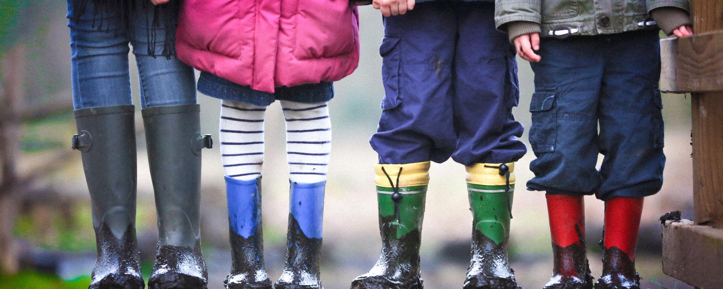 four children standing together. the picture focuses on the children's galoshes and coats