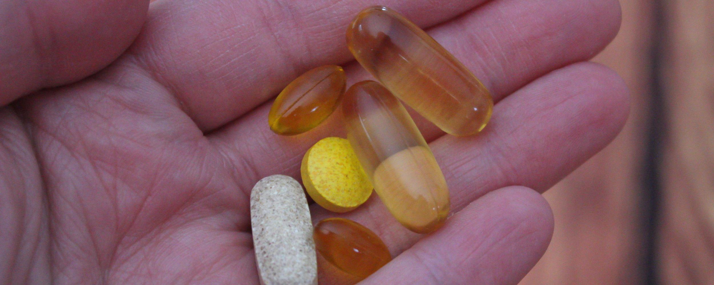 picture of a hand holding different pills and vitamins