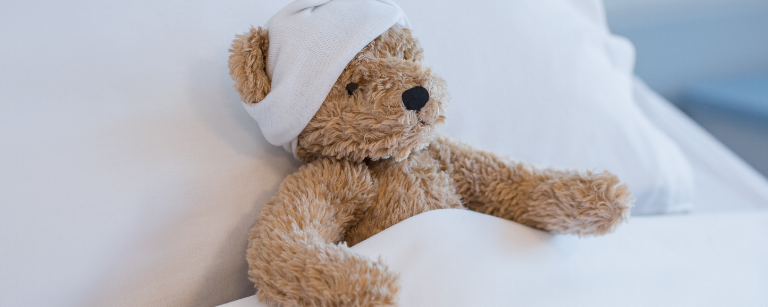 Teddy Bear tucked into bed with a bandage on it's head.
