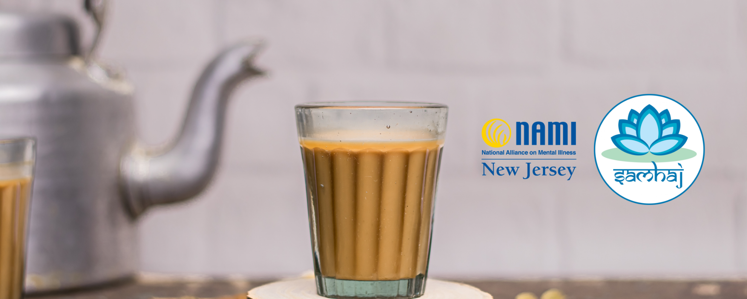 Picture of a kitchen countertop with Indian chai in glass cup on top of a wooden coaster in the foreground, a metal kettle and other masalas to make tea in the background, and the NAMI NJ and SAMHAJ logos superimposed on the right side of the picture.