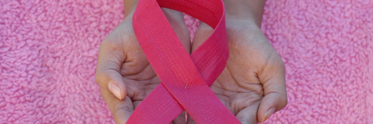 a pair of hands holding a pink ribbon 