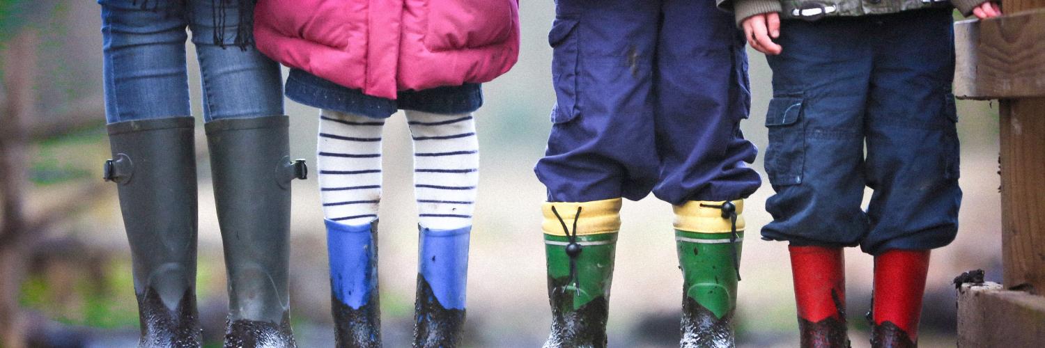 four children standing together. the picture focuses on the children's galoshes and coats