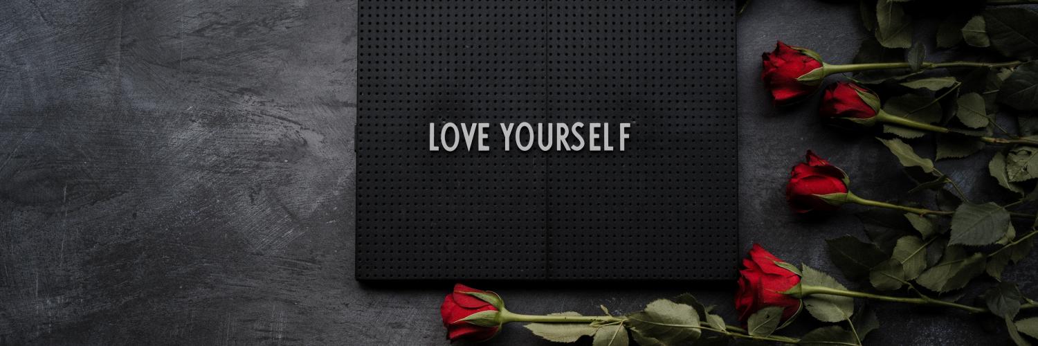 a slate with the text "Love Yourself" on it with red roses stacked next to the slate
