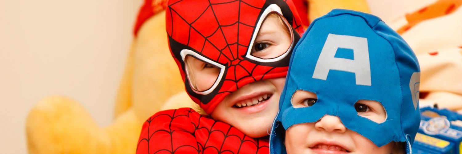 two children, one dressed as Spiderman, and another as Captain America, smile at the camera