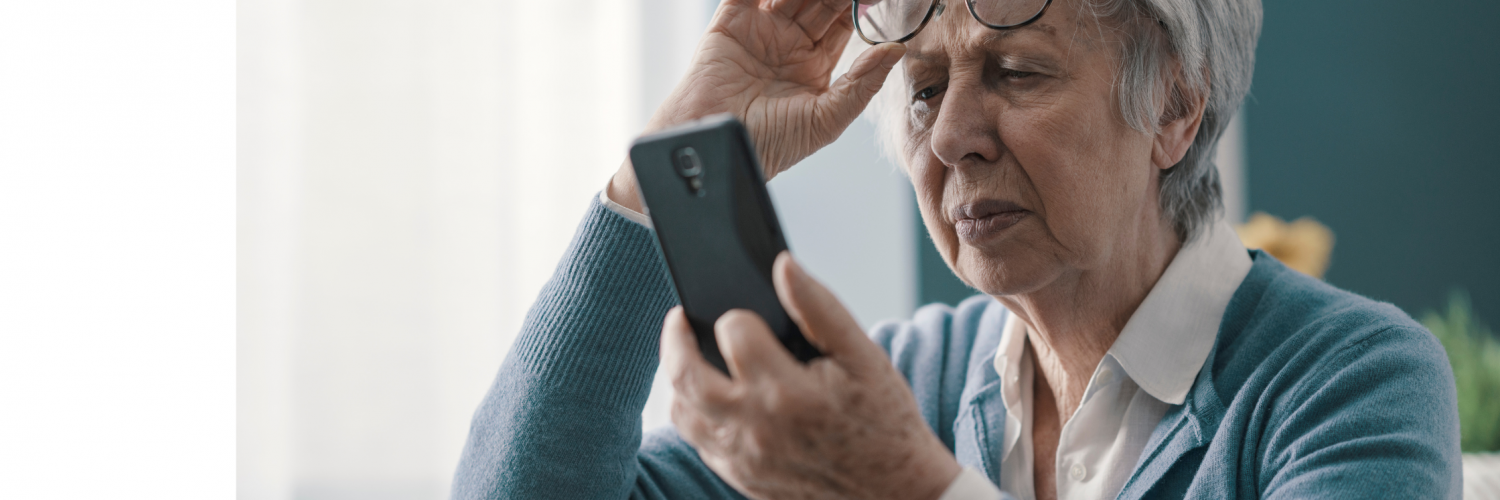 Elderly woman removing her reading glasses to see her cell phone screen.