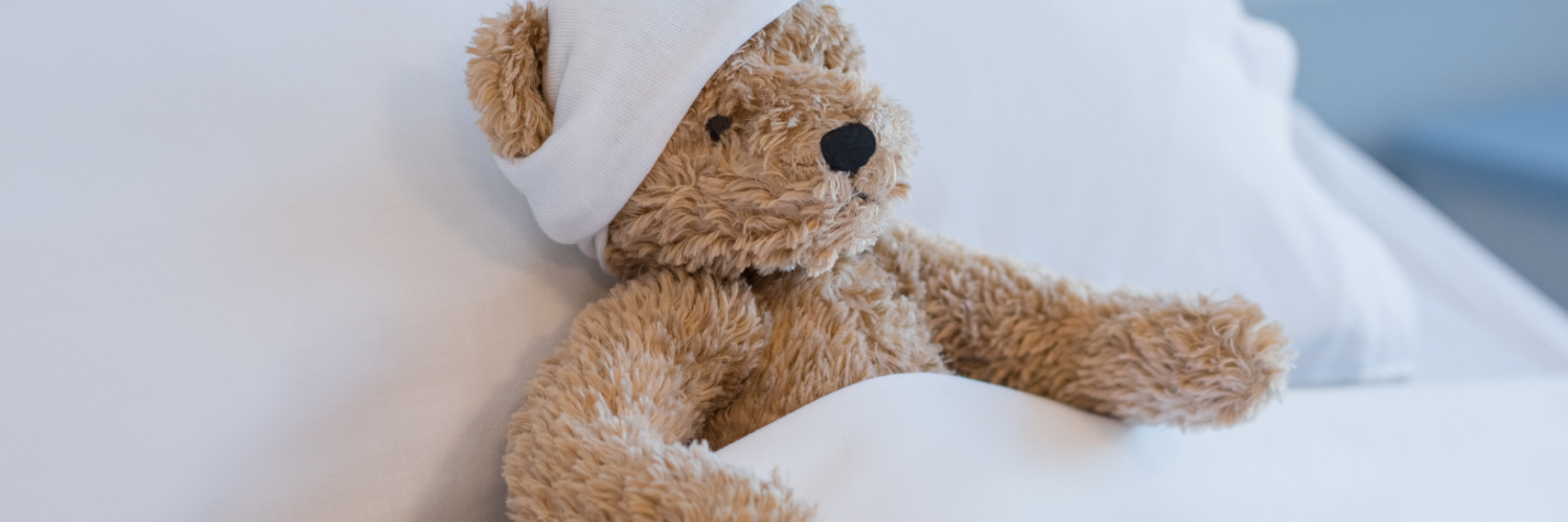 Teddy Bear tucked into bed with a bandage on it's head.