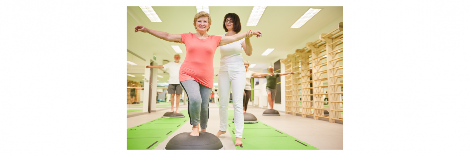 Trainer helps senior woman with balance training on the Bosu Ball in a fitness class