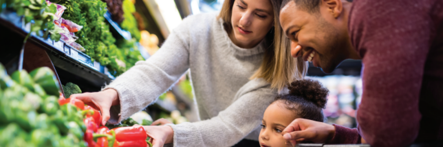 two adults and a child at a supermarket looking at vegetables